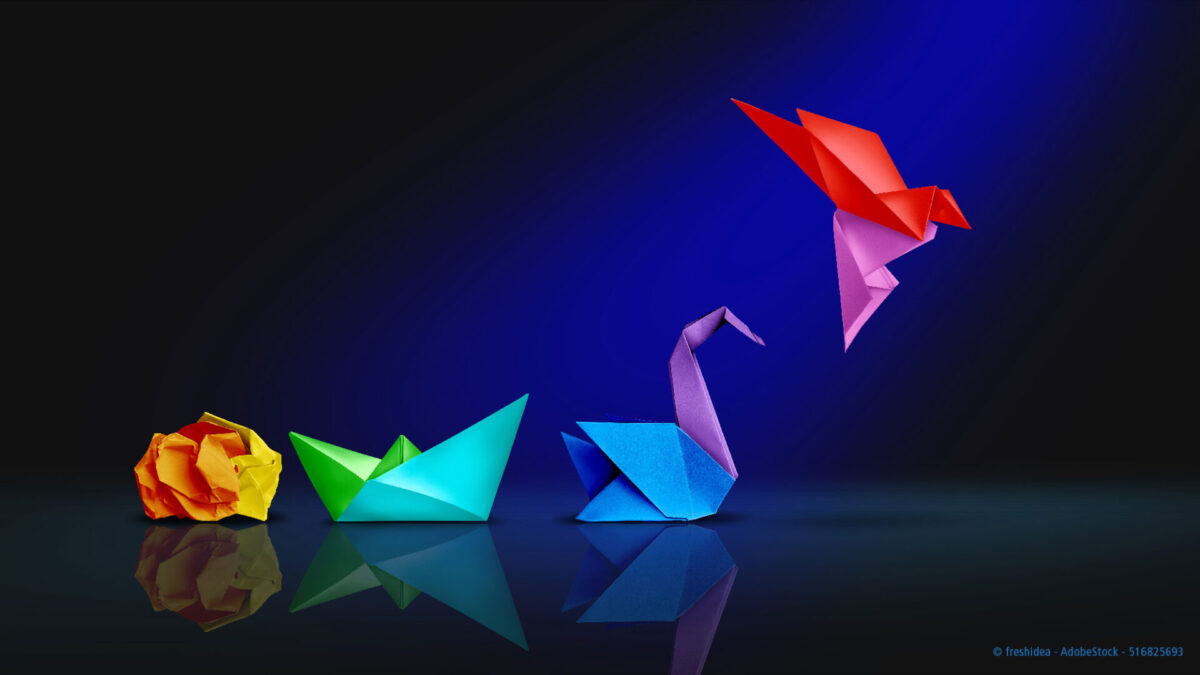 Vier farbenfrohe Origami-Figuren - eine gelbe Rose, ein grünes Boot, ein blauer Schwan und ein rot-rosa Vogel - sind auf einer reflektierenden Oberfläche mit einem blauen Scheinwerfer angeordnet.